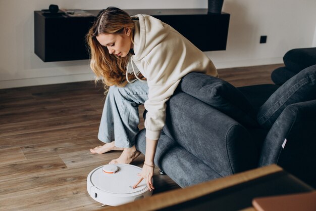 Frau zu Hause beobachtet Roboterstaubsauger beim Aufräumen des Hauses