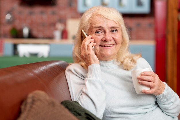 Frau zu Hause, die Tee trinkt und Telefon verwendet