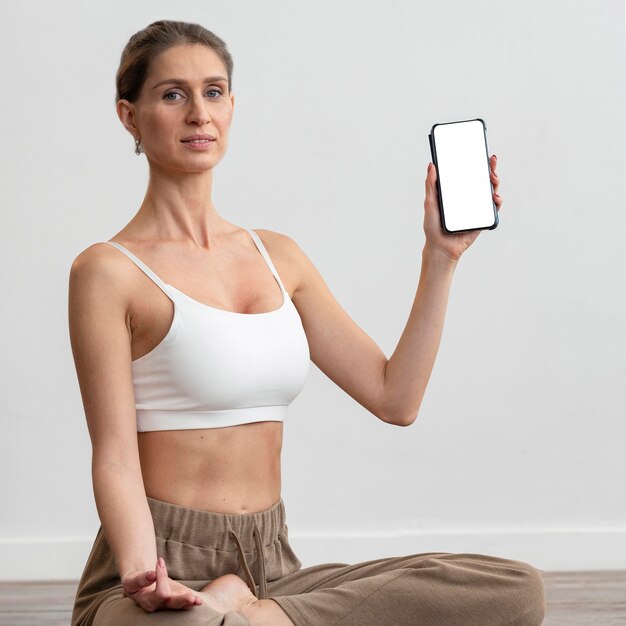Frau zu Hause, die Yoga macht und Smartphone hält