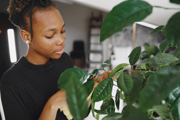 Frau zu Hause. Mädchen in einem schwarzen Pullover. Afrikanerin benutzt den Lappen. Person mit Blumentopf.