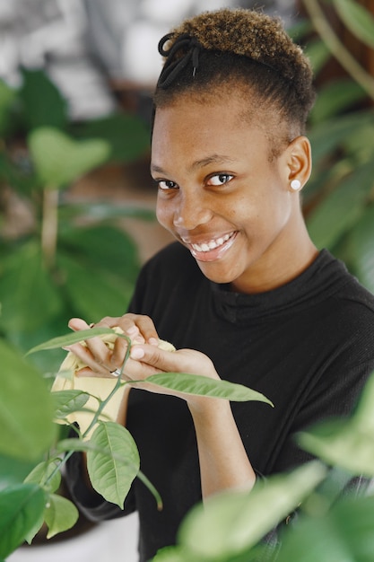 Frau zu Hause. Mädchen in einem schwarzen Pullover. Afrikanerin benutzt den Lappen. Person mit Blumentopf.