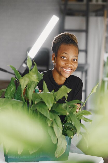 Frau zu Hause. Mädchen in einem schwarzen Pullover. Afrikanerin im Büro. Person mit Blumentopf.