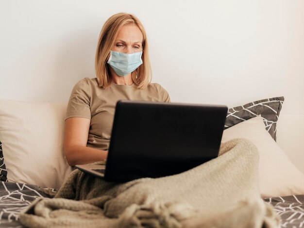 Frau zu Hause mit medizinischer Maske und Laptop