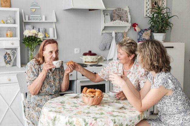 Frauen der multi Generation, die Hörnchen mit Kaffee während des Frühstücks genießen