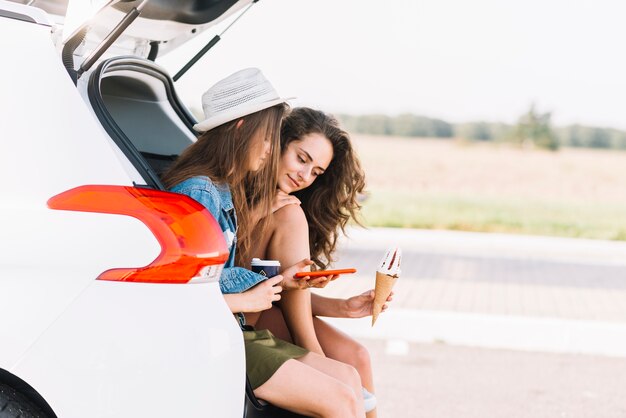 Frauen, die auf Autokofferraum auf Feldhintergrund sitzen