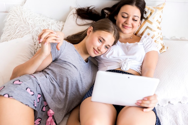 Kostenloses Foto frauen, die auf bett mit tablette sitzen