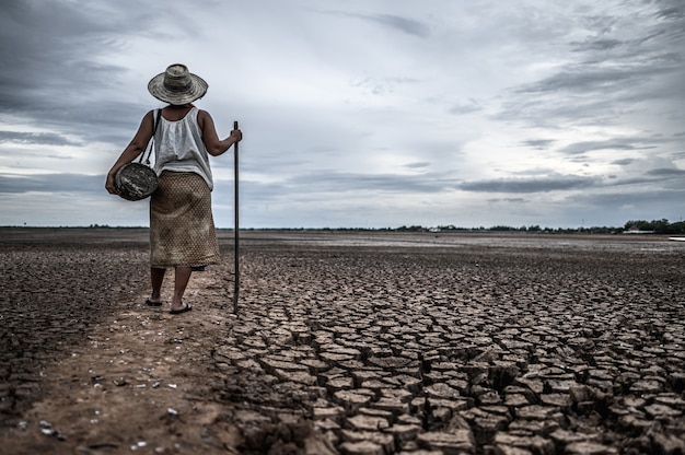 Frauen, die auf trockenem Boden und Fischereiausrüstung, globaler Erwärmung und Wasserkrise stehen