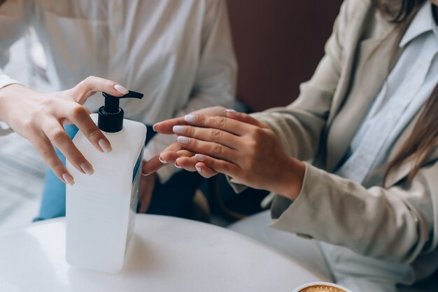 Frauen, die ein antibakterielles Antiseptikum verwenden, um im Café zu desinfizieren. Neue soziale Regeln nach Pandemiekonzept.