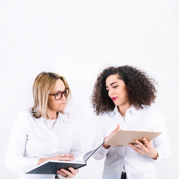 Frauen, die Informationen im Notizbuch und in der Tablette suchen