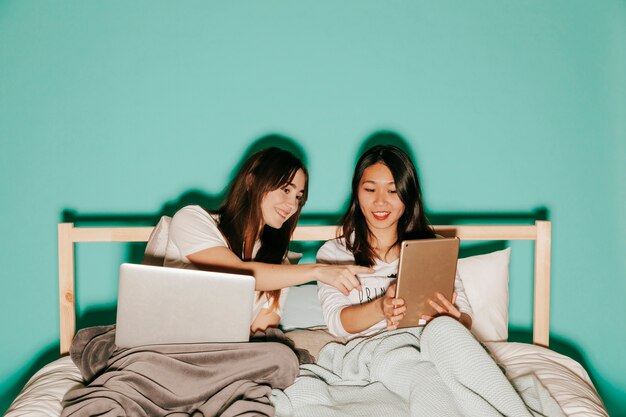 Frauen, die Laptop und Tablette im Bett durchstöbern