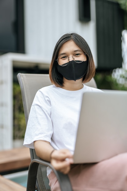 Frauen, die Masken tragen und Laptops am Pool spielen.