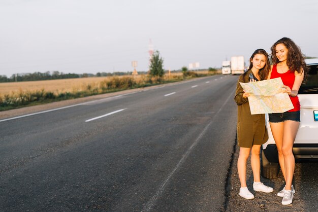 Frauen, die nahes weißes Auto mit Karte stehen