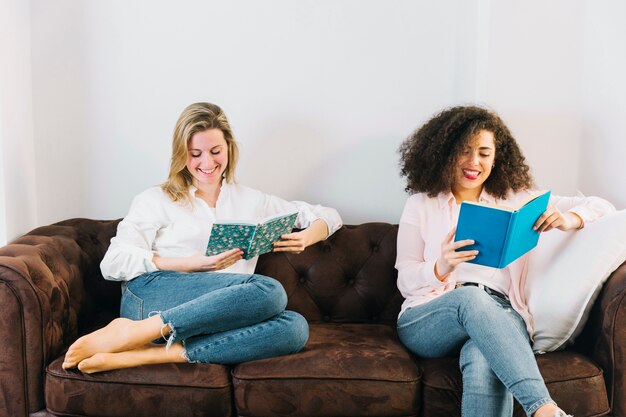 Frauen, die nette Bücher auf Sofa lesen