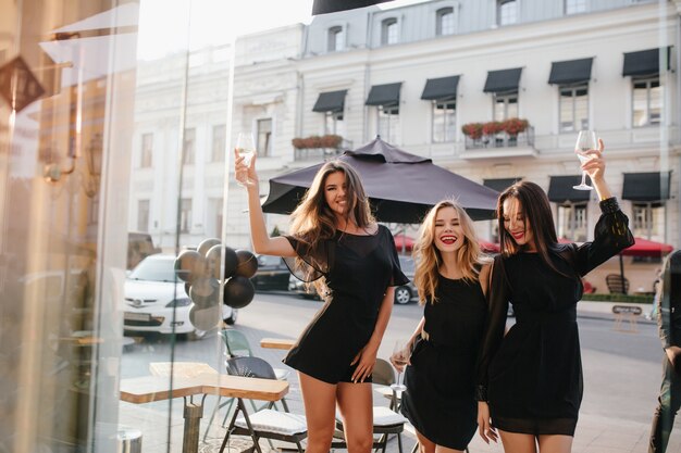 Frauen im schwarzen Kleid mit langen Ärmeln, die ein Glas Wein heben und lachen