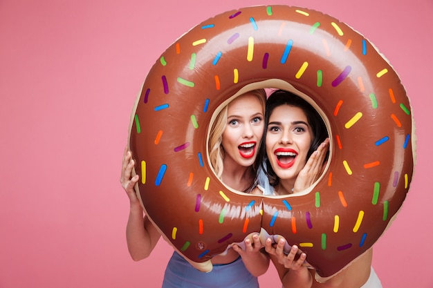 Frauen in Strandkleidung, die Spaß mit Donut geformter Herzmatratze haben