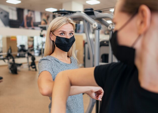 Frauen mit medizinischen Masken, die den Ellbogengruß im Fitnessstudio üben