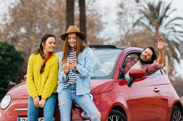 Frauen mit Smartphone nahe dem Mann, der sich heraus vom Auto lehnt