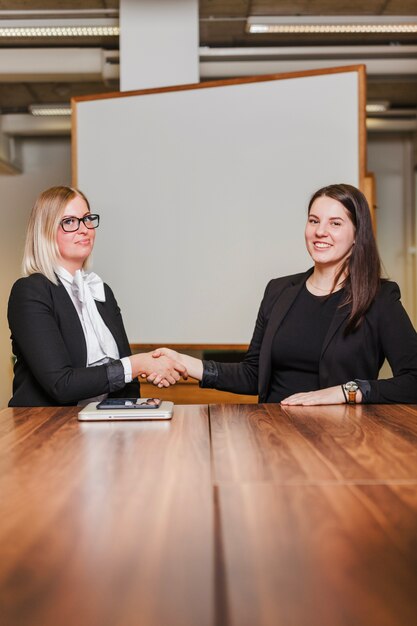 Frauen sitzen am Tisch Händeschütteln lächelnd