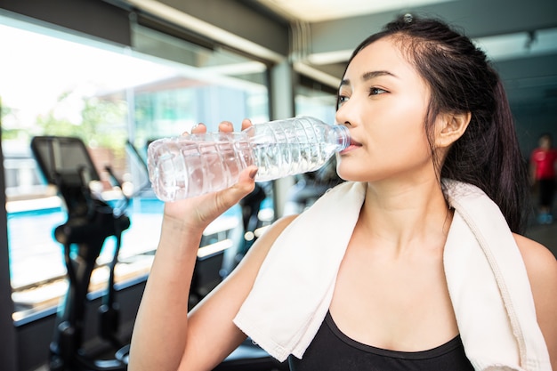 Frauen trinken nach dem Training Wasser aus Flaschen und Taschentüchern im Fitnessstudio.