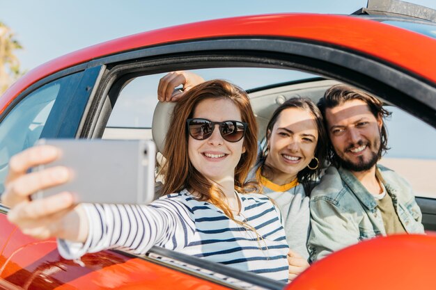 Frauen und positiver Mann, die selfie auf Smartphone im Auto nehmen