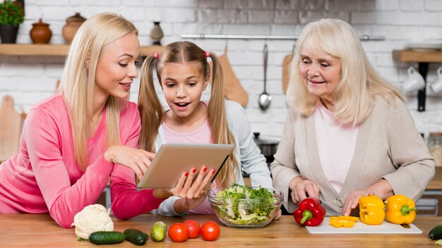 Frauen, welche die Tablette in der Küche betrachten