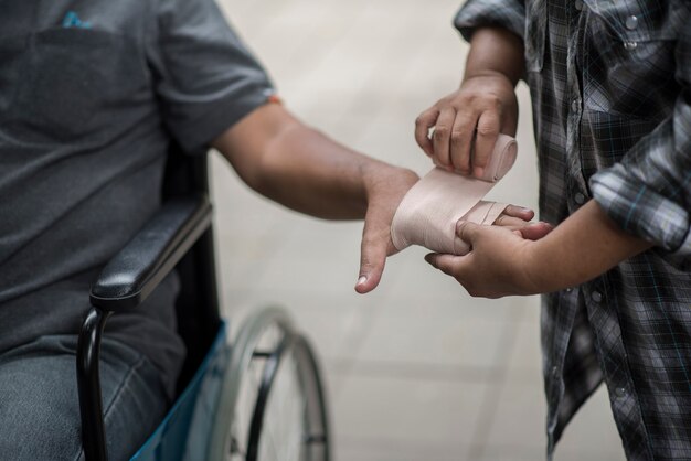 Frauen wickeln Hände auf Männer ein, die auf Rollstuhlpatienten mit Verbänden sitzen.