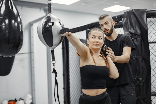 Frauenboxen. Anfänger im Fitnessstudio. Dame in schwarzer Sportbekleidung. Frau mit Trainer.