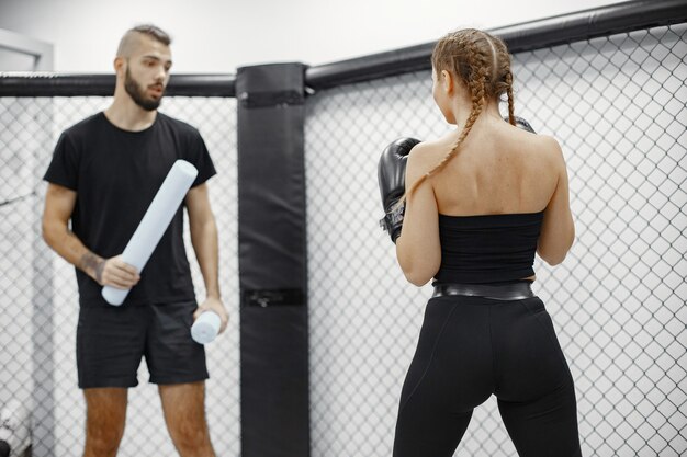 Frauenboxen. Anfänger im Fitnessstudio. Dame in schwarzer Sportbekleidung. Frau mit Trainer.