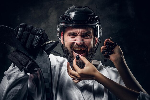 Frauenhände mit präziser Maniküre füttern einen brutalen emotionalen Hockeyspieler mit schwarzer Traube.