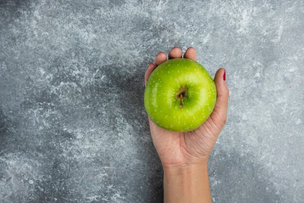 Frauenhand, die Apfel auf Marmor hält.