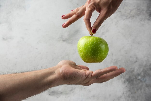 Frauenhand, die Apfel zur Mannhand gibt.