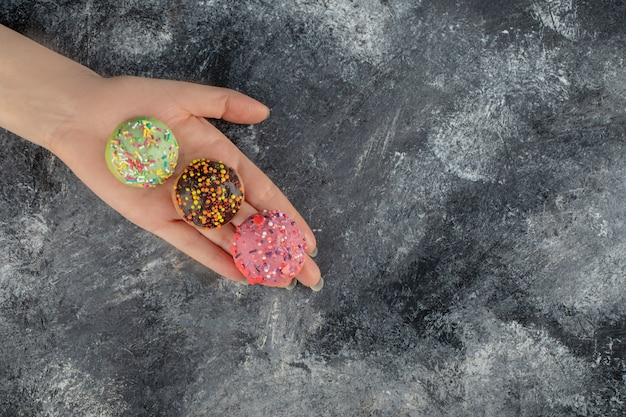 Frauenhand, die bunte süße donuts mit streuseln hält.