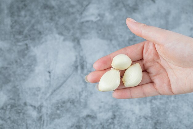 Frauenhand, die einen Knoblauch auf einem bunten Hintergrund hält.