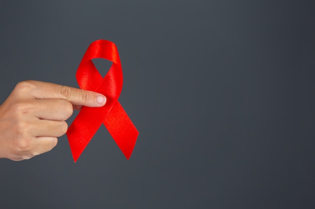 Frauenhand, die HIV-Bewusstseinskonzept des roten Bandes Welt-AIDS-Tag und Welttag der sexuellen Gesundheit hält.