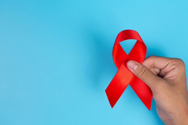 Frauenhand, die HIV-Bewusstseinskonzept des roten Bandes Welt-AIDS-Tag und Welttag der sexuellen Gesundheit hält.