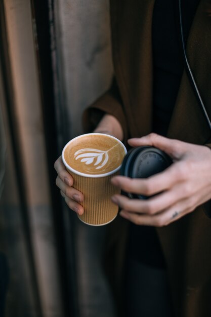 Frauenhand, die Kaffee mit Latte Art auf einem grauen Teller von oben erreicht. Holztisch im Hipster-Café. Vintage Farbfiltereffekt.