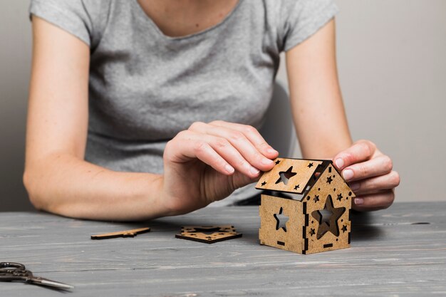 Frauenhand, die kreatives kleines Haus auf Holztisch macht