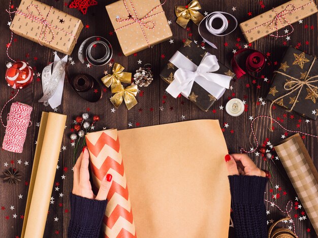 Frauenhand, die Rolle des Packpapiers für das Verpacken der Weihnachtsgeschenkbox ausbreitet