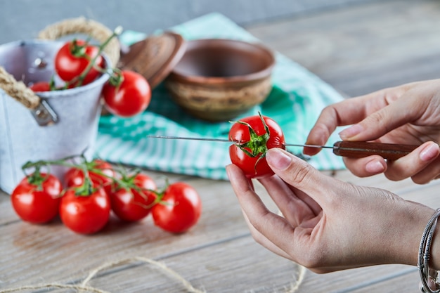 Frauenhand, die rote Tomate mit Messer in zwei Stücke schneidet