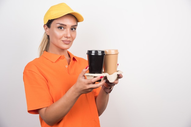 Frauenkurier, der zwei Tassen Kaffee auf weißer Wand hält.
