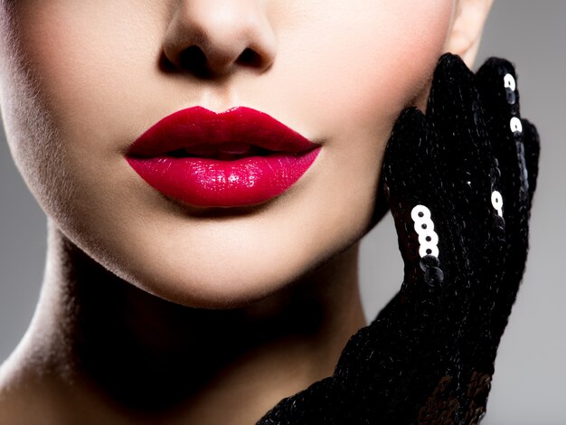 Frauenlippen mit rotem Lippenstift und schwarzen Handschuhen auf der Wange schließen