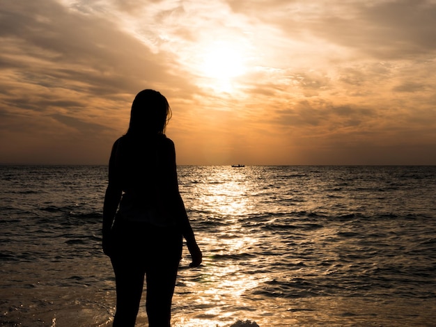 Frauensilhouette, die Sonne am Strand bei Sonnenuntergang beobachtet. Touristisches Mädchen im Strandurlaub