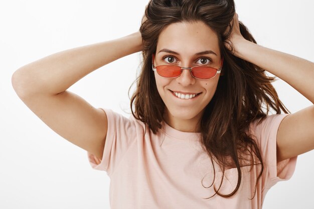 Freches attraktives Mädchen mit Sonnenbrille, die gegen die weiße Wand aufwirft