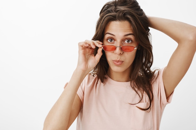 Freches attraktives Mädchen mit Sonnenbrille, die gegen die weiße Wand aufwirft