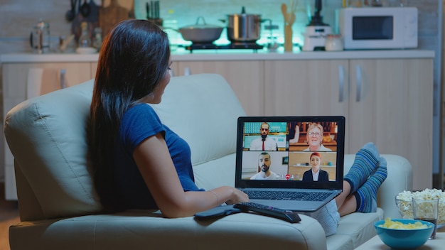 Freiberuflerin mit Web-Chat-Konferenz auf dem Sofa im Wohnzimmer. Remote-Mitarbeiter diskutieren bei Online-Meetings, beraten sich mit Kollegen per Videoanruf und Webcam, die vor dem Laptop arbeiten