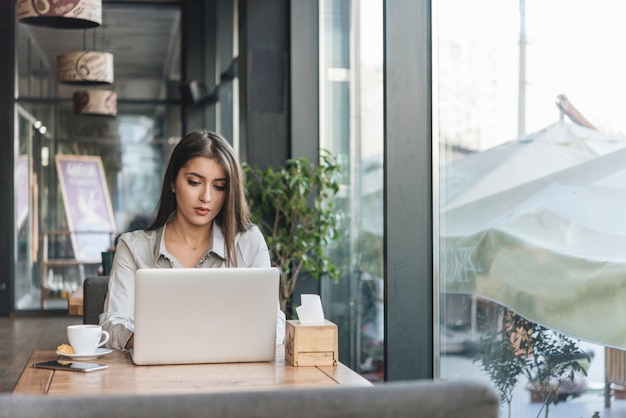 Freiberuflich tätige Frau, die mit Laptop in der Kaffeestube arbeitet