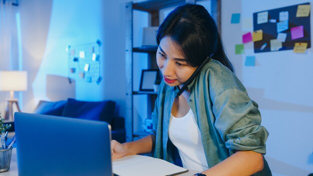 Freiberufliche asiatische Frauen, die Laptop verwenden, sprechen am Telefon beschäftigter Unternehmer, der entfernt im Wohnzimmer arbeitet.