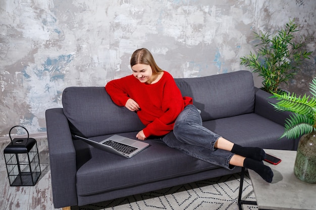 Freiberufliche frau, die auf einem sofa in einem gemütlichen zuhause sitzt und aus der ferne an einem modernen laptop arbeitet, erfahrene frau, die online-webinare auf der website ansieht. arbeiten von zu hause während der quarantäne