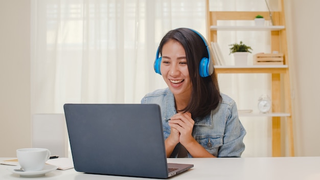 Freiberufliche Geschäftsfrauen-Freizeitkleidung unter Verwendung einer Laptop-Arbeitsanruf-Videokonferenz mit Kunden am Arbeitsplatz im Wohnzimmer zu Hause. Glückliches junges asiatisches Mädchen entspannen sitzen auf Schreibtisch erledigen Arbeit im Internet.
