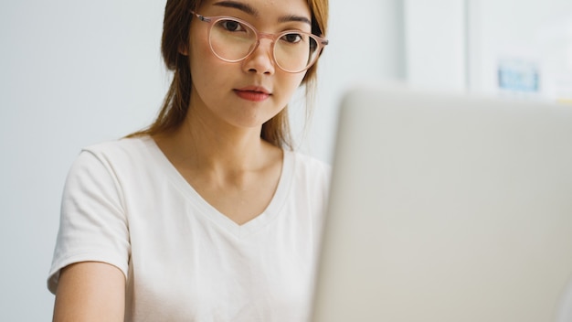 Freiberufliche junge asiatische Geschäftsfrau Freizeitkleidung mit Laptop im Wohnzimmer zu Hause arbeiten.